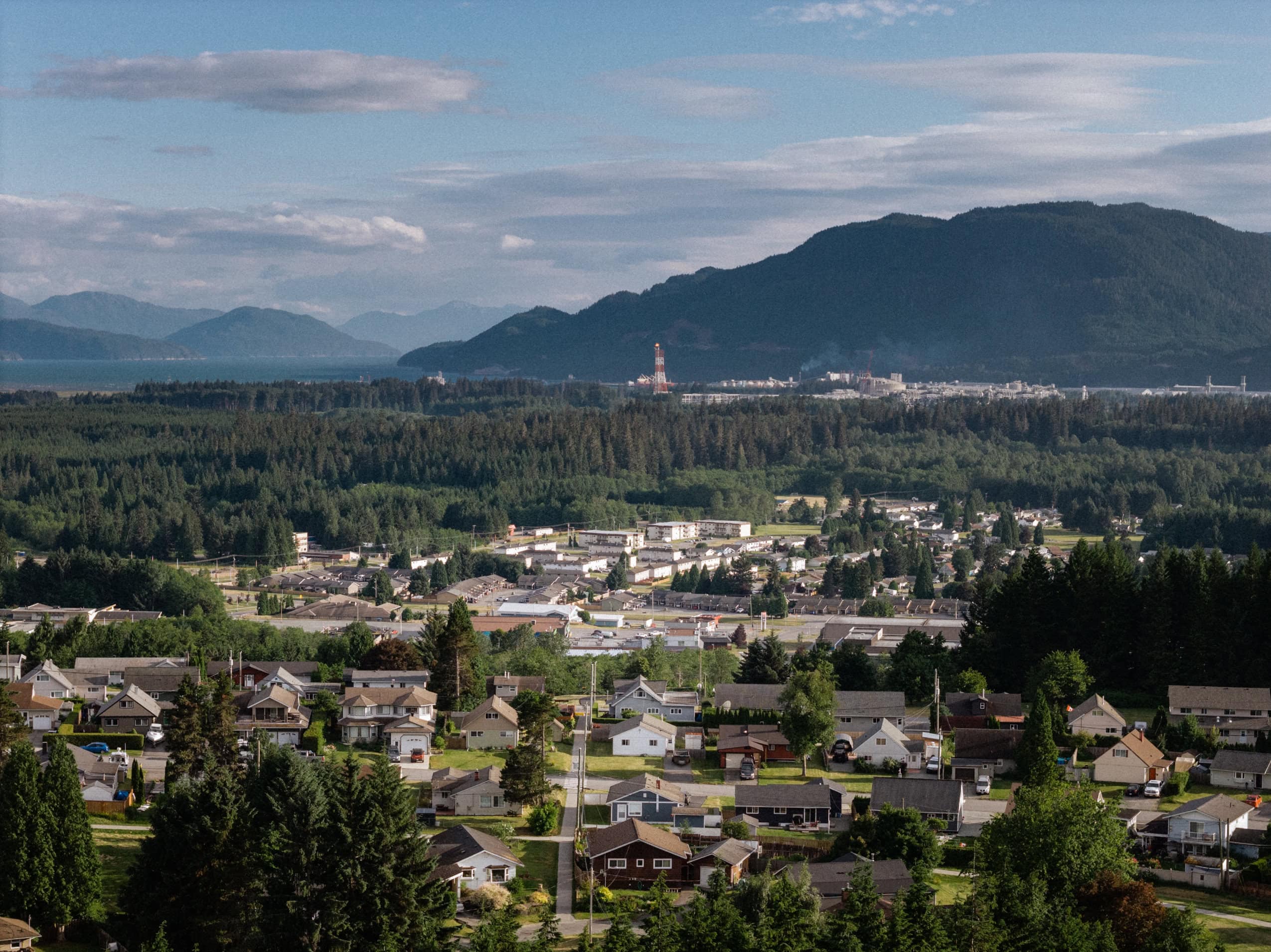 The town of Kitimat with houses and trees in the foreground and LNG Canada in the background.