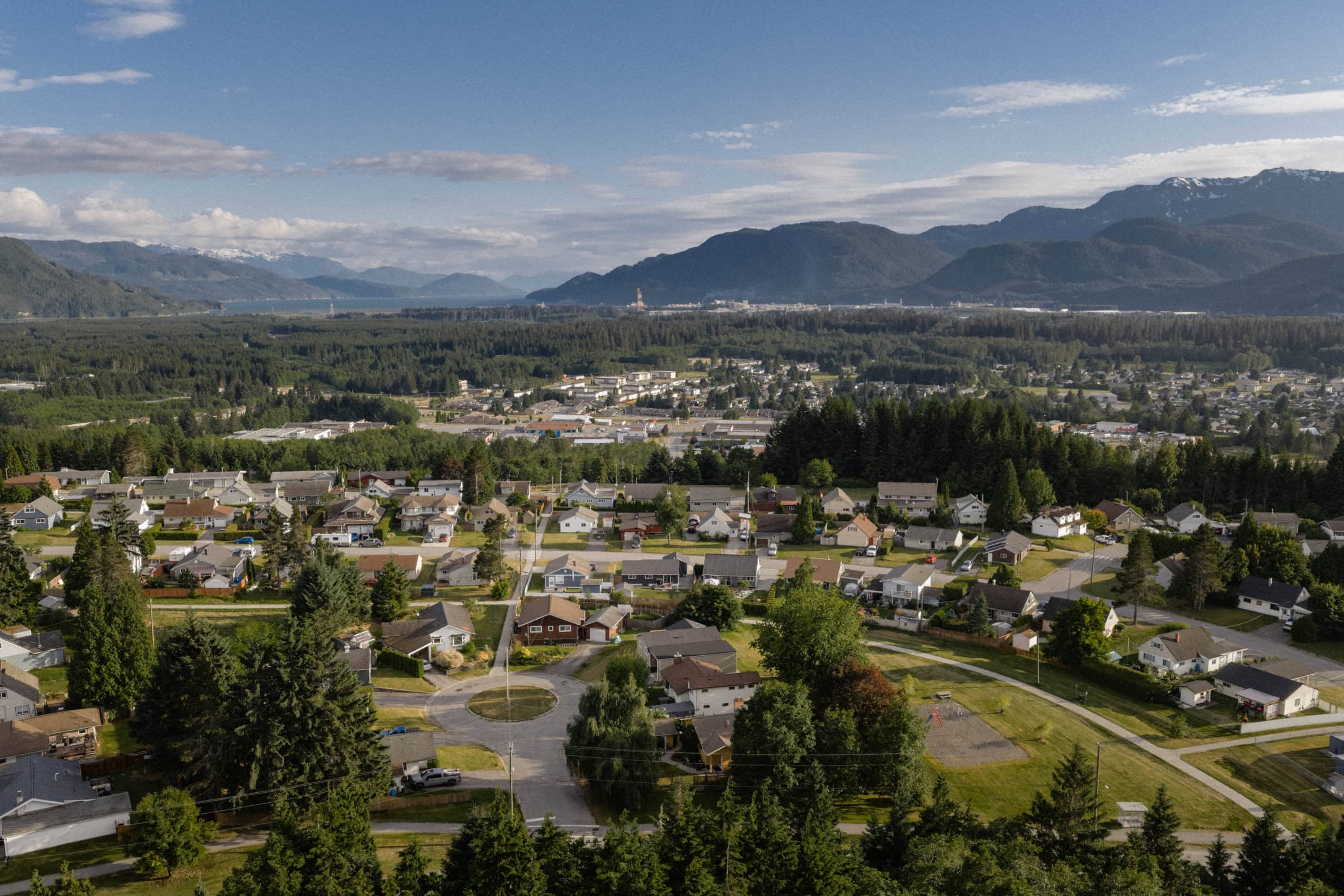 The town of Kitimat with houses and trees in the foreground and LNG Canada in the background.