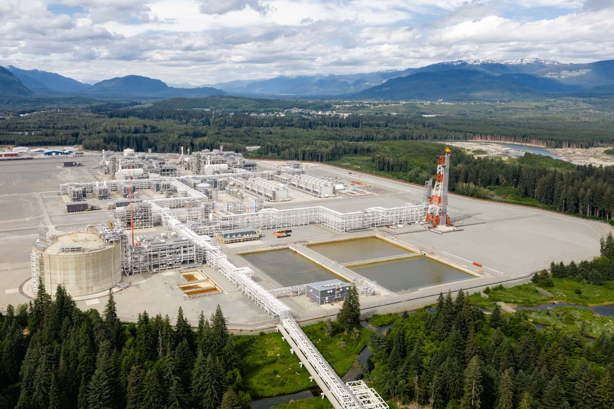 LNG Canada, a large industrial facility sits in the middle of the frame surrounded by green grass a river and mountains