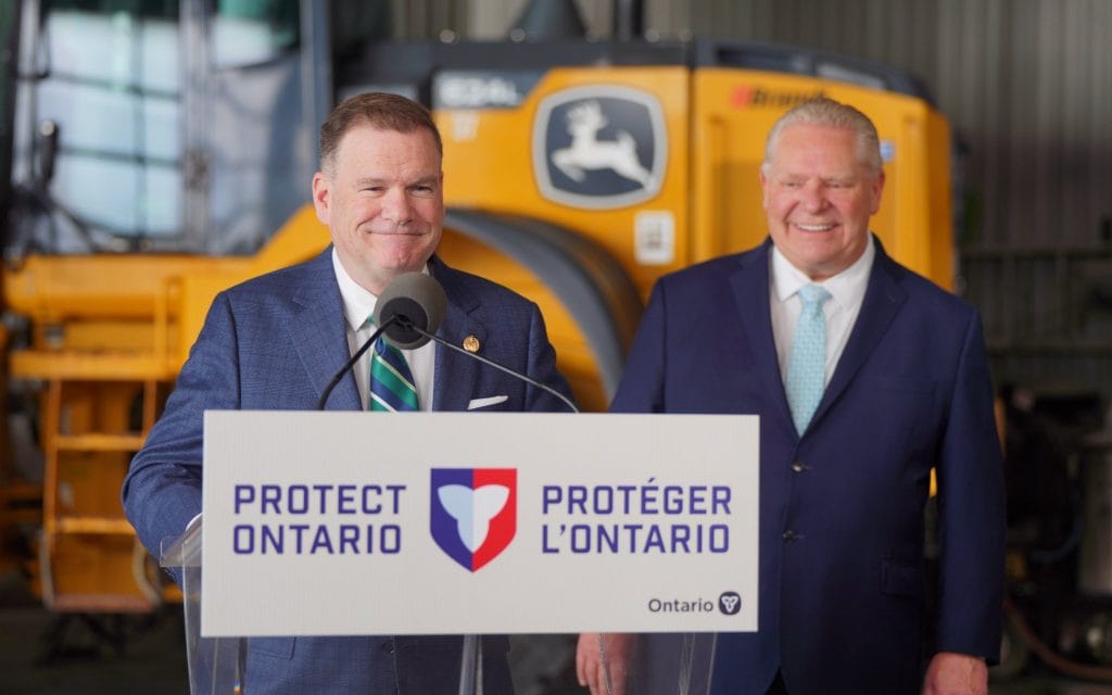 Two men stand behind a podium that says "Protect Ontario" on it in English and French