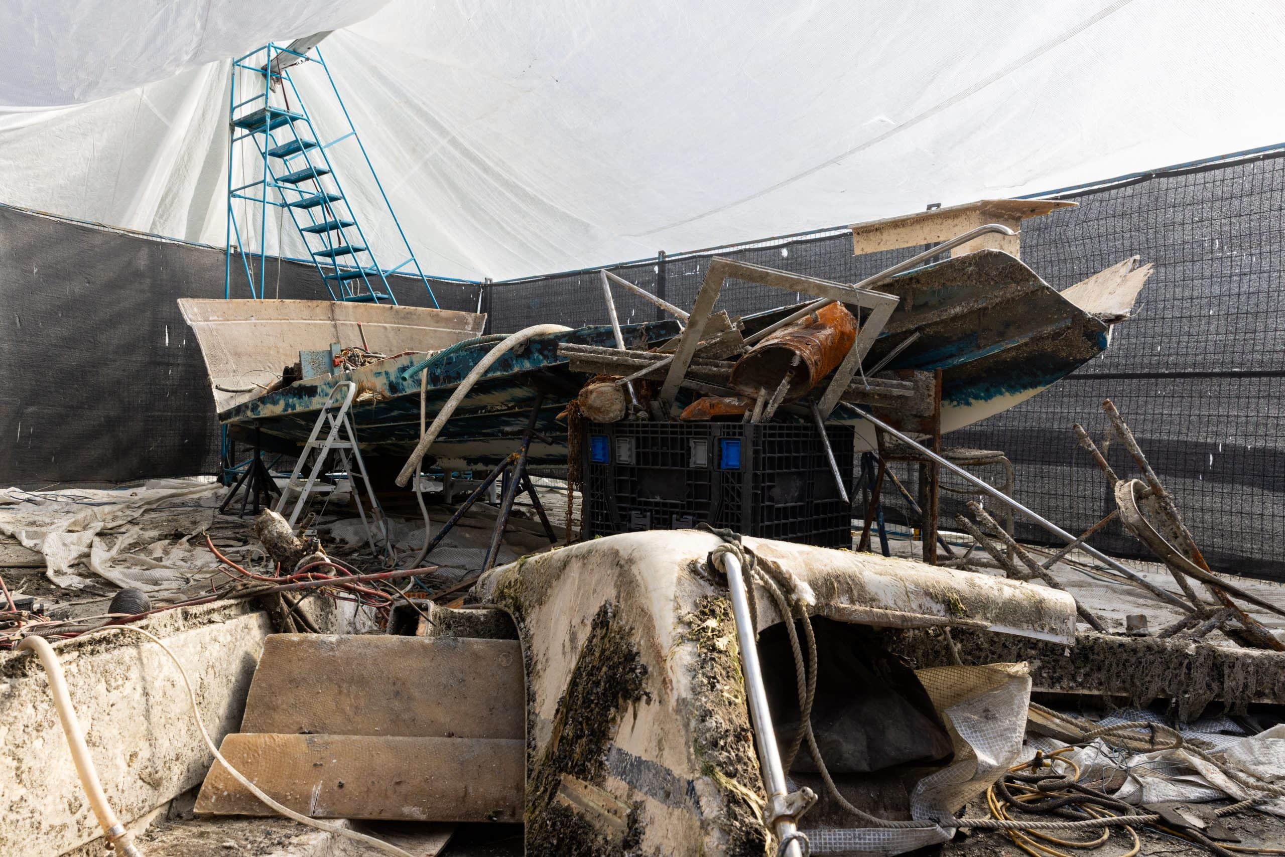 Boat wreckage that has been hauled ashore, including broken and dirty pieces of the hull and steps.