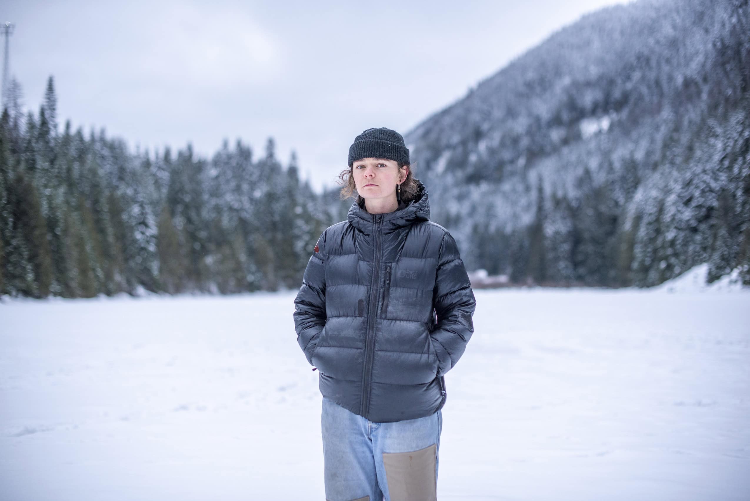 Kari Medig stands in front of a frozen lake with snow-covered forest surrounding it.