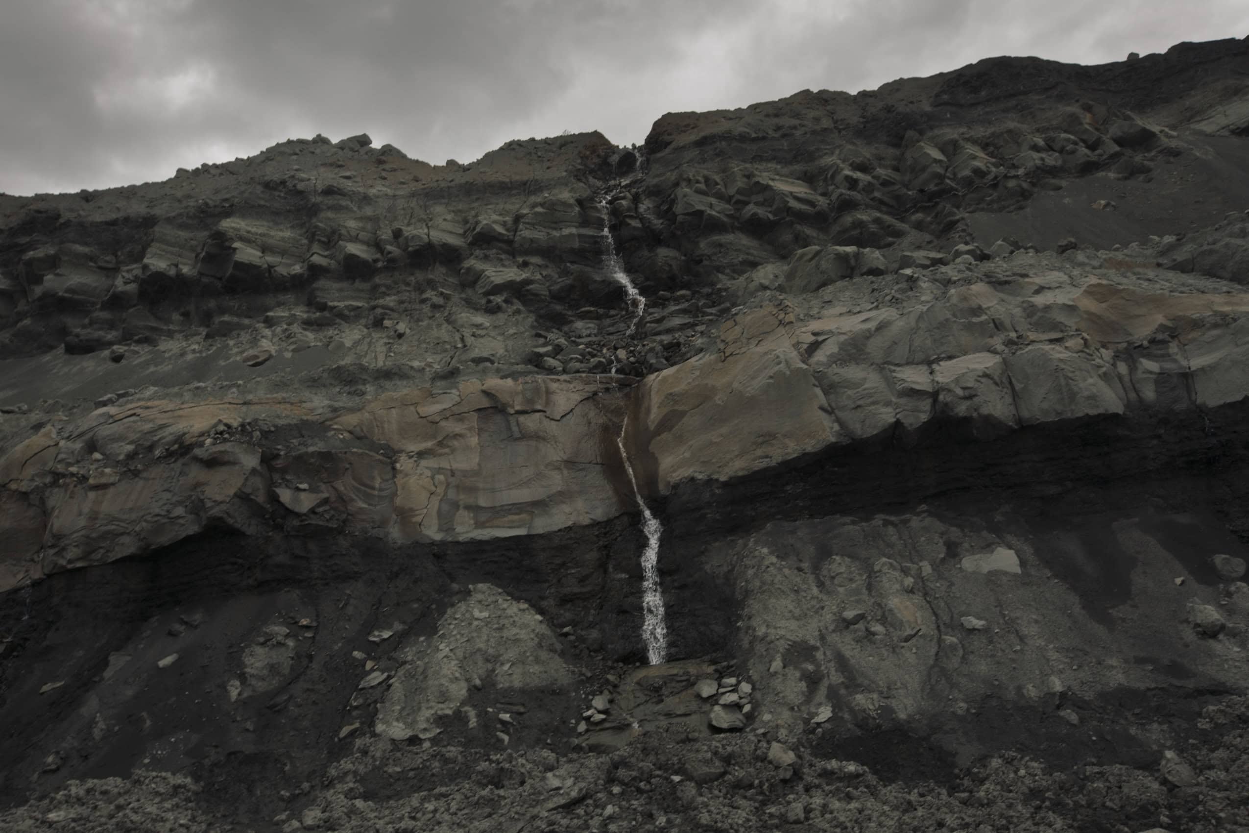The rocky side of an open-pit coal mine, with a stream of water running down it.
