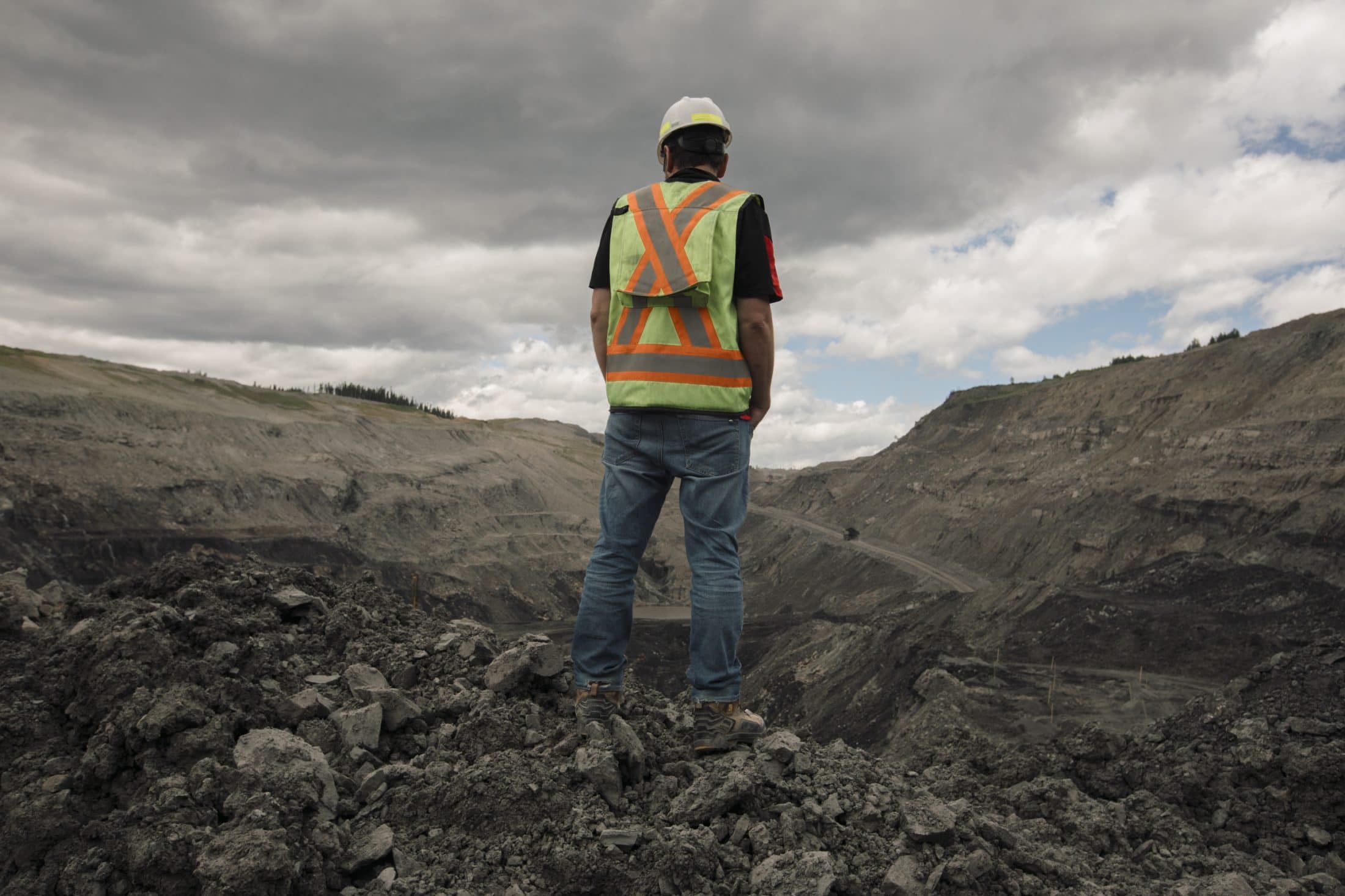A worker wearing a hard hat, reflective vest and jeans overlooks mine operations at the Coal Valley mine south of Edson, Alberta.