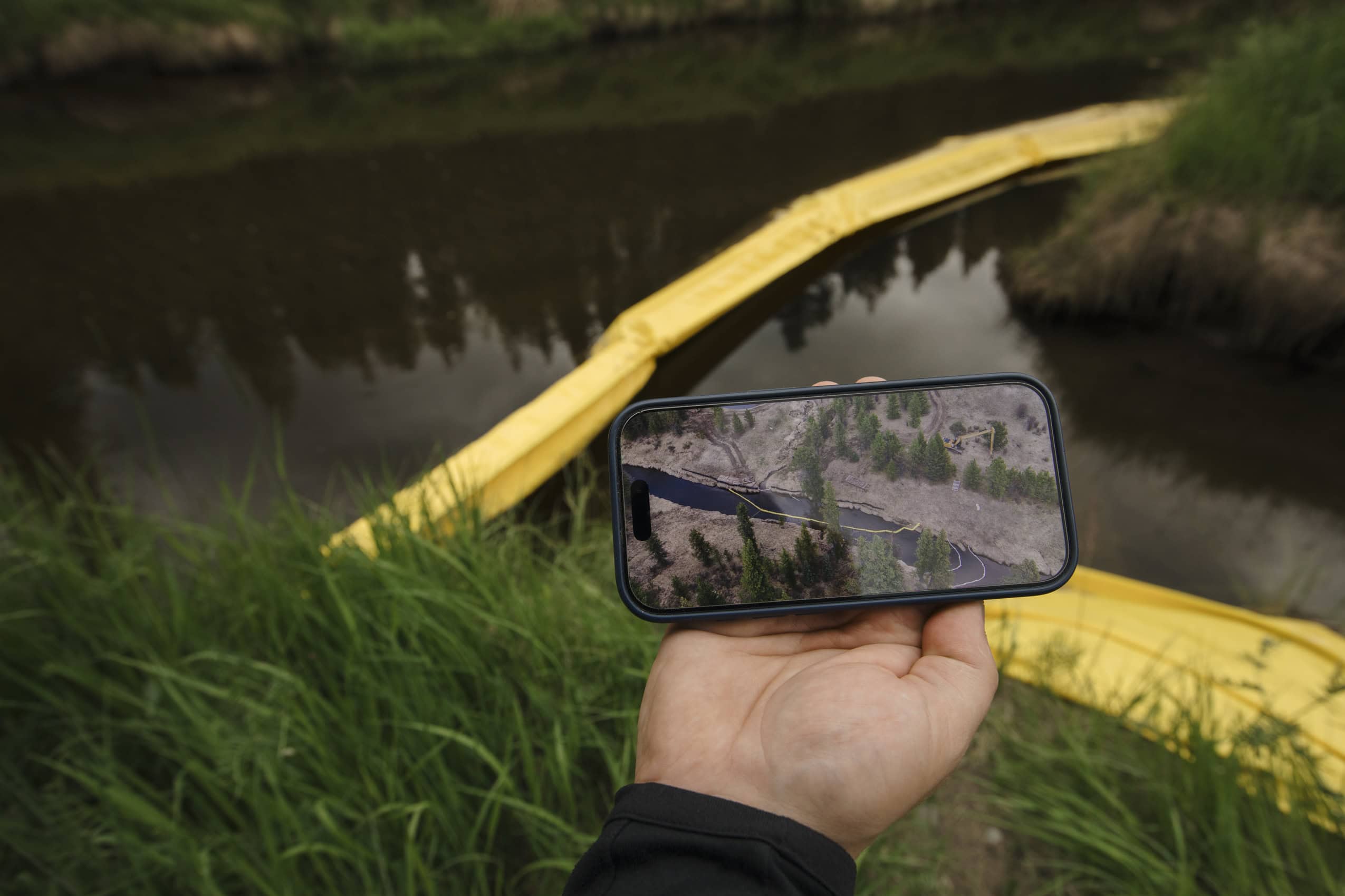 A hand holds a smartphone that is displaying a picture of yellow "curtains" used to isolate fish from a watercourse.