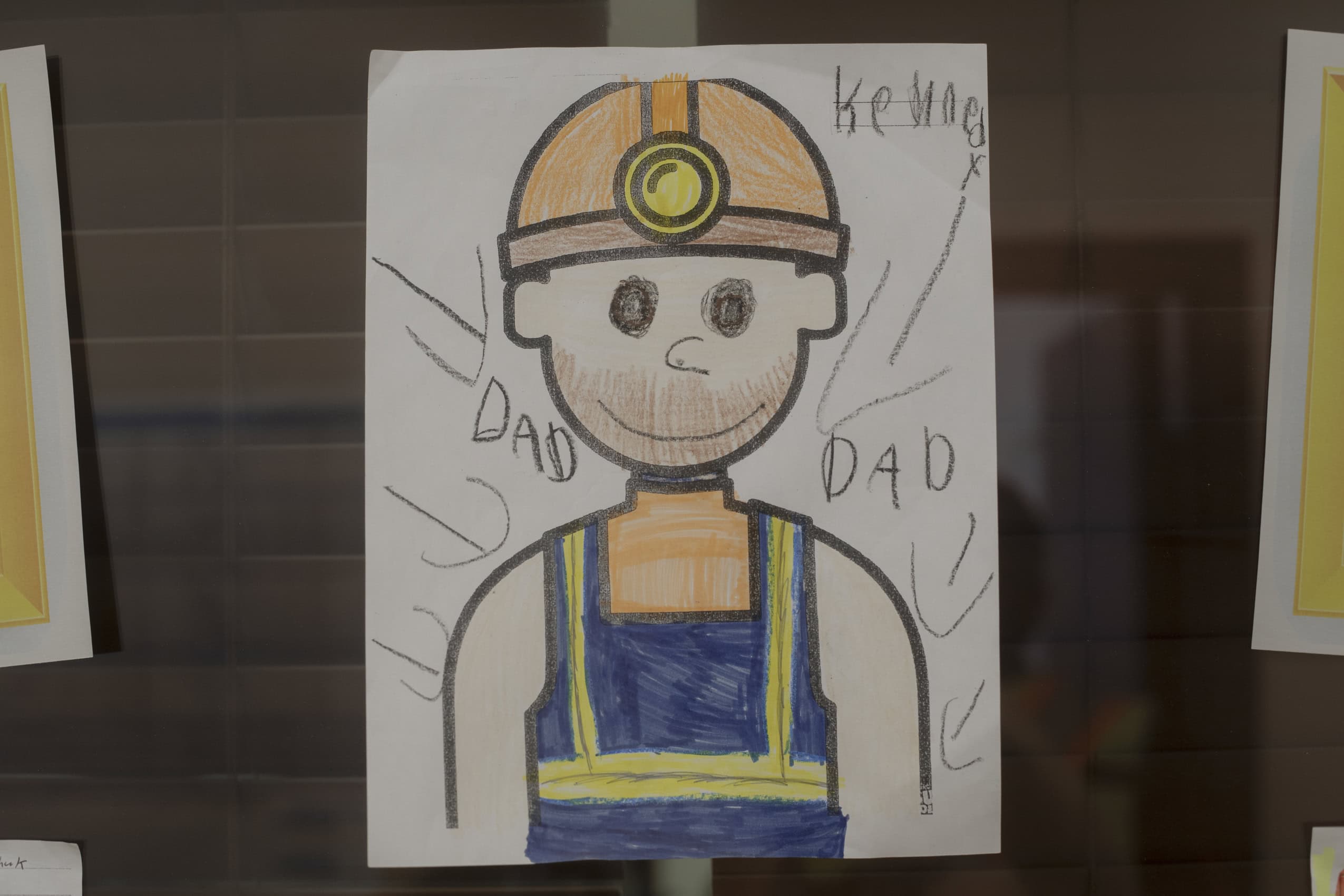 A child's drawing of a worker wearing a hard hat and reflective vest with a label reading, "Dad."