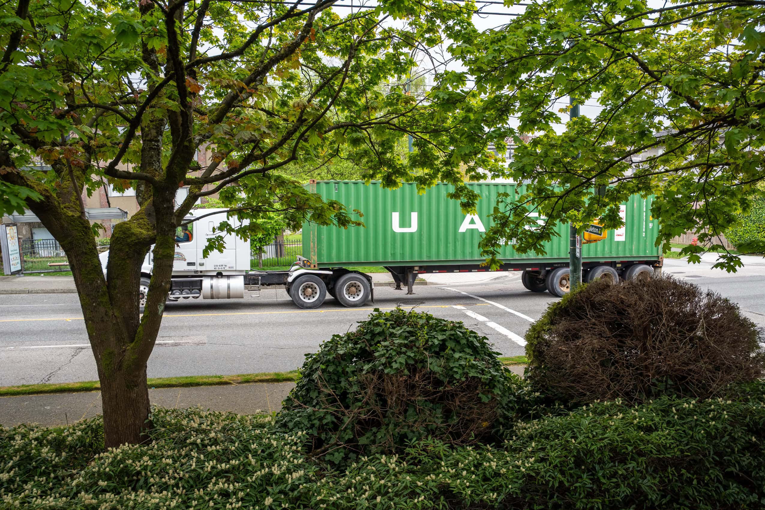 A U-Haul truck driving along a multi-lane city road, viewed from a home's window.