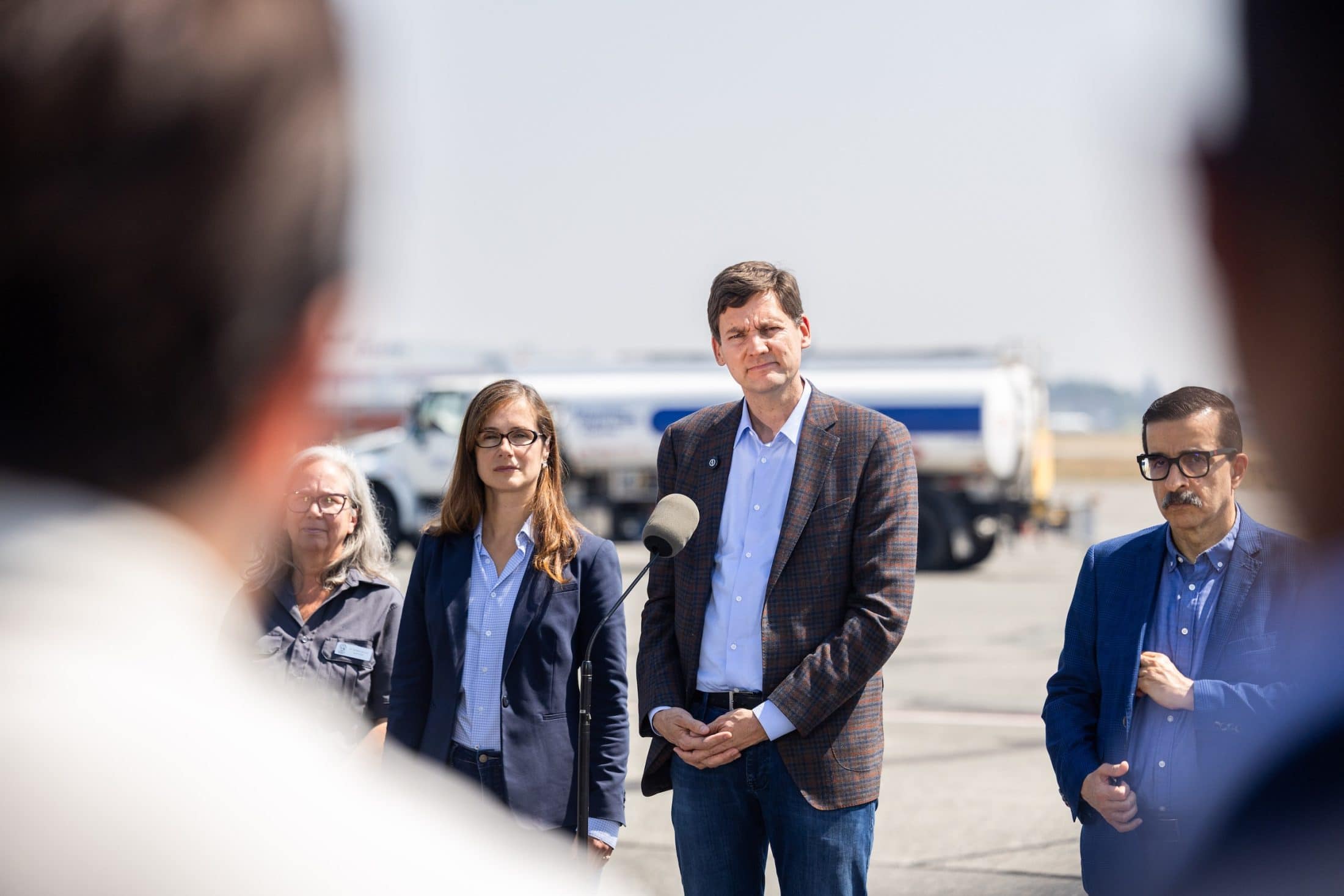 B.C. Premier David Eby is standing on airport tarmac speaking into a microphone.
