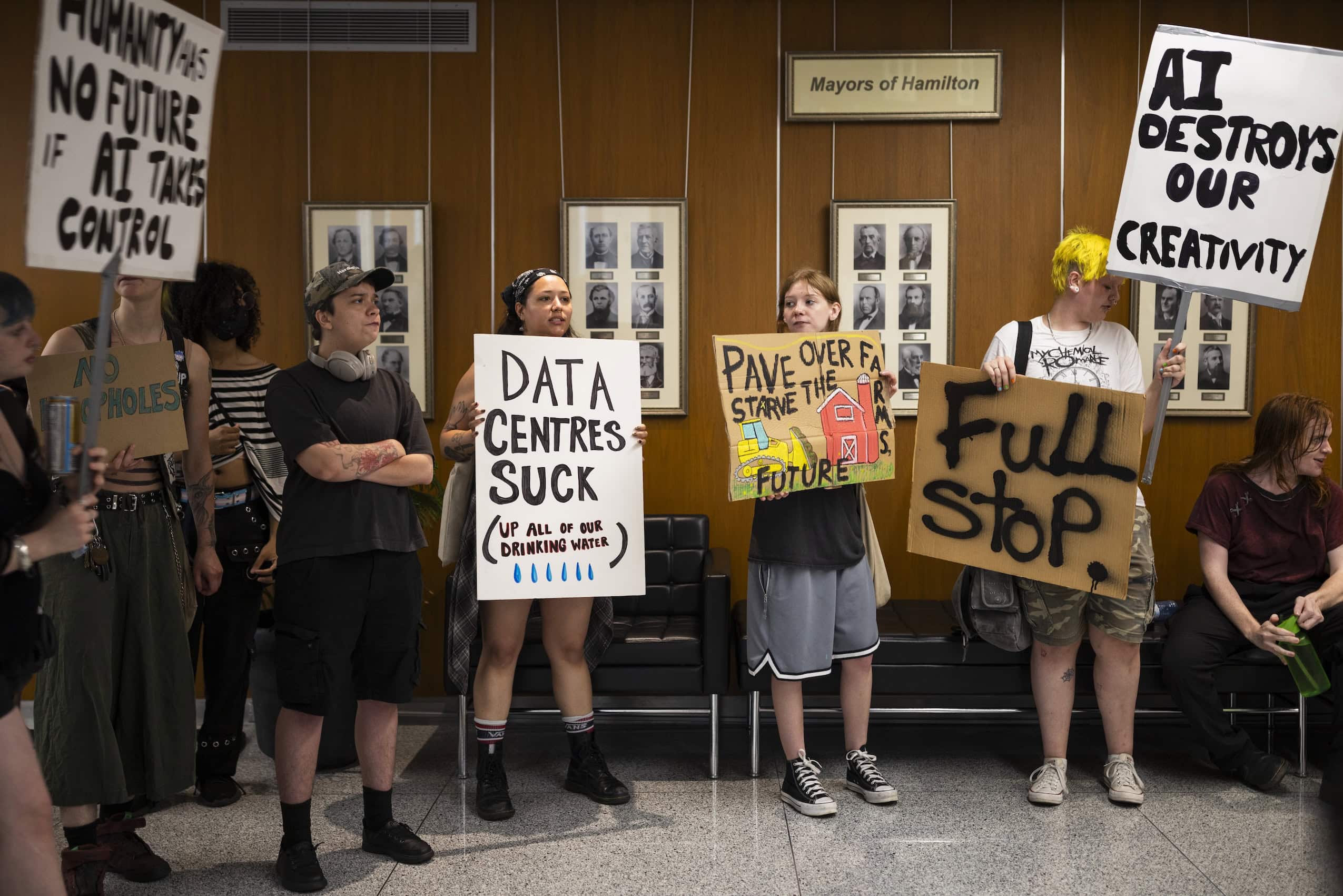 Demonstrators in opposition to A.I. data centres are seen holding signs inside Hamilton's city hall.