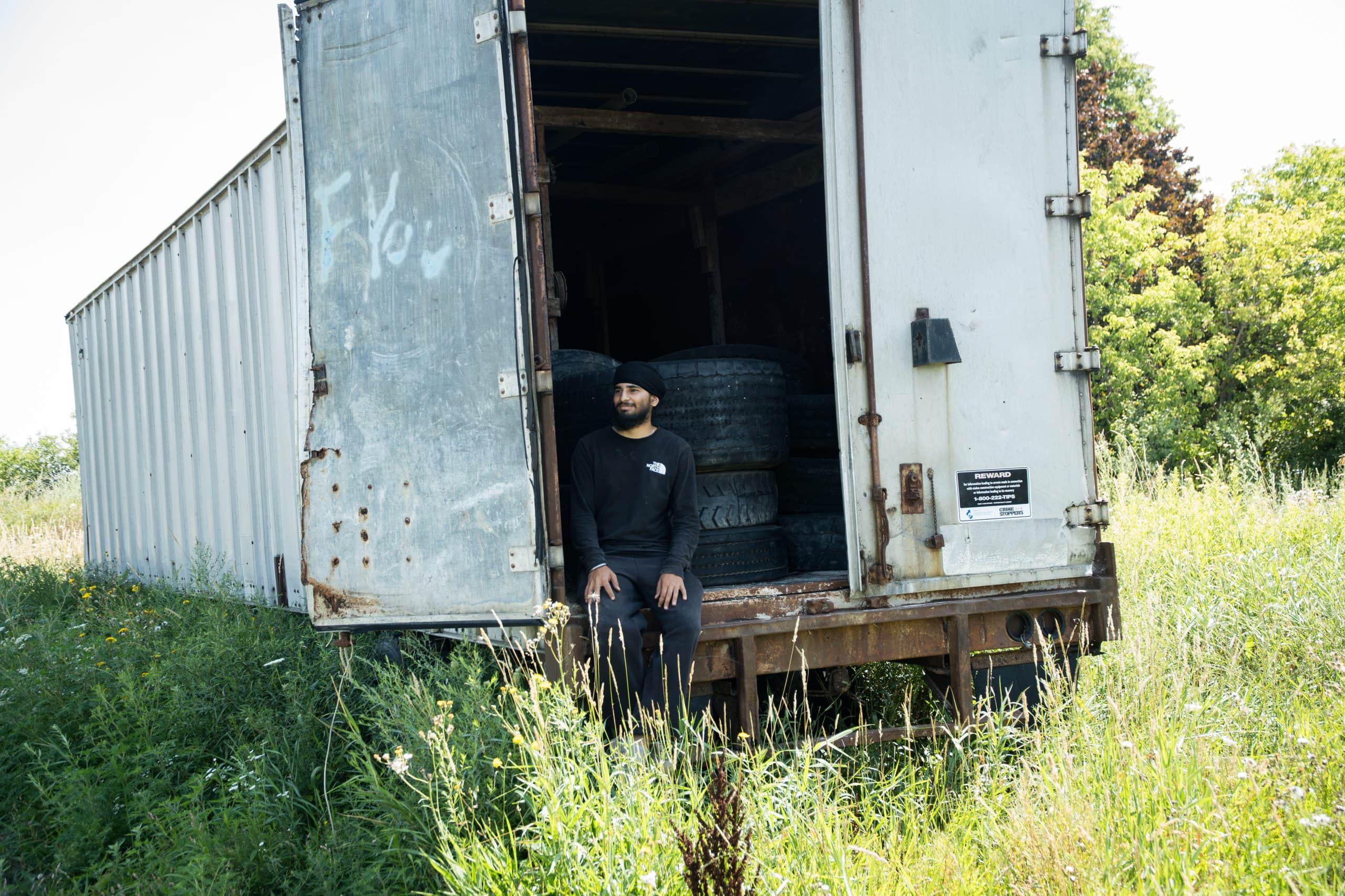 A young man in a turban sits inside a truck trailer full with tires