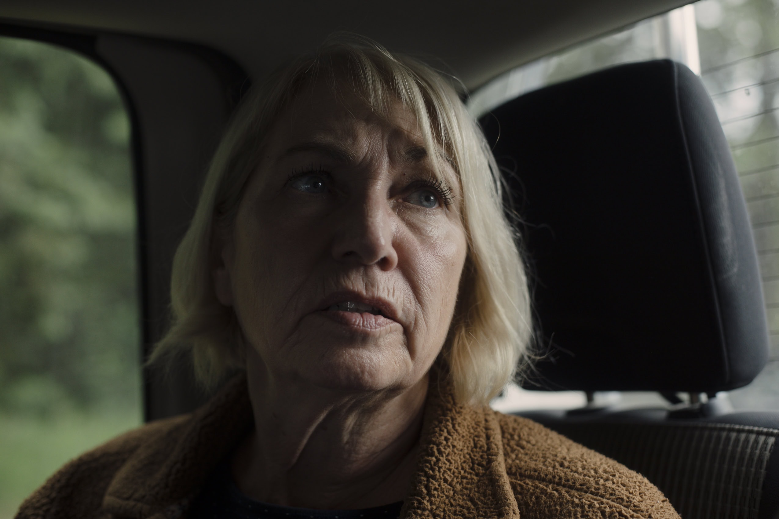 A close up photo of a woman's face, shadowed as she sits in the back of a truck.