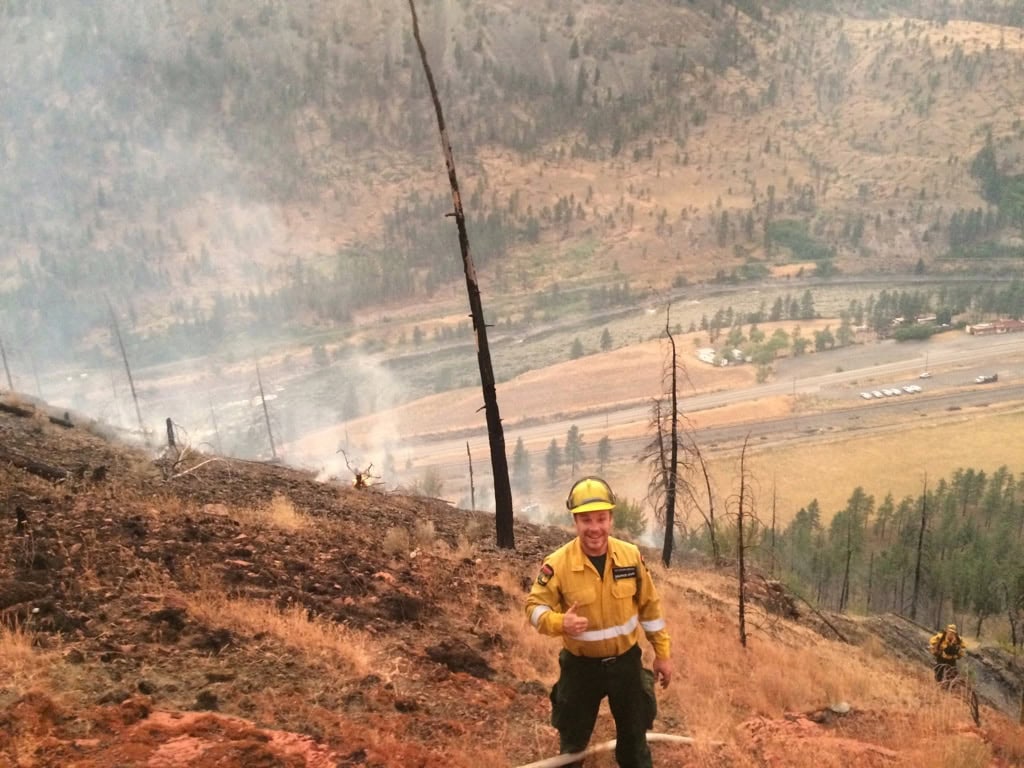 Wildland firefigther Matthew Brackenreed smiles and gives a thumbs up on the top of a hill damaged by fire.