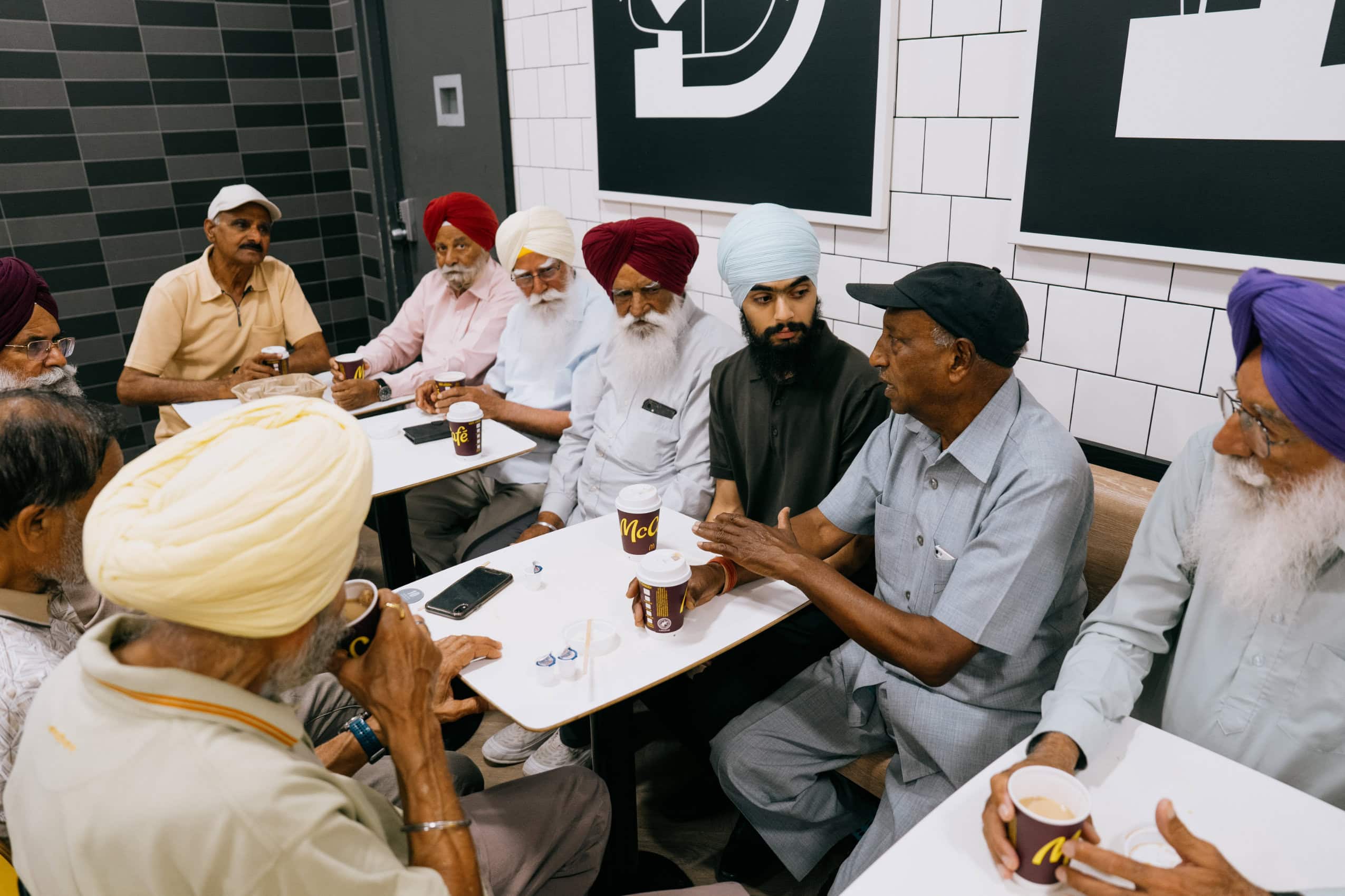 A group of men are seated at tables at a McDonald's, drinking coffee and chatting.