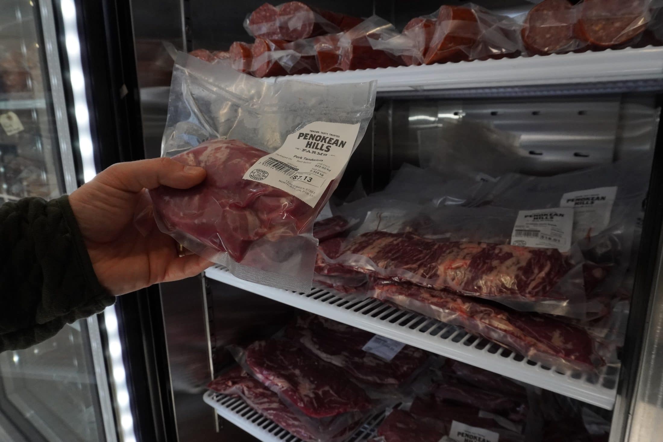 A hand selects a bag of packaged meat from a shop freezer.