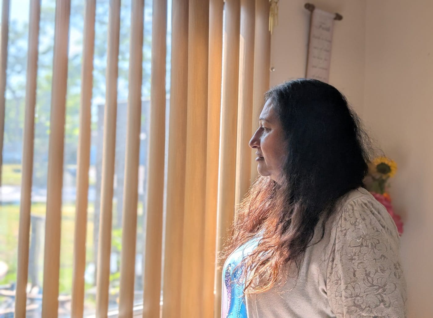 A woman is standing inside her home and looking outside a window