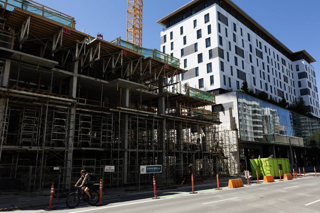 A street view of a multi-unit building under construction in downtown Victoria. Beside it is a new looking multi-unit building, with white cladding