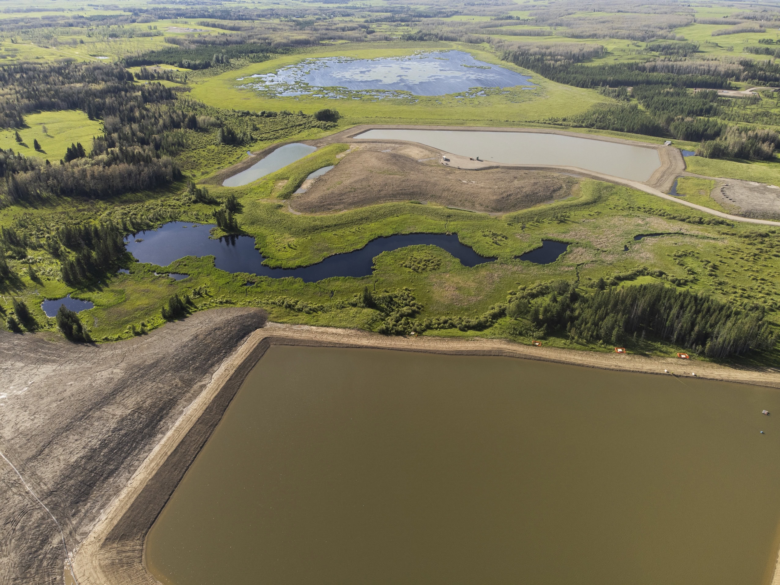An aerial shot, looking down on two large water reservoirs that bissect a wetland in Alberta.