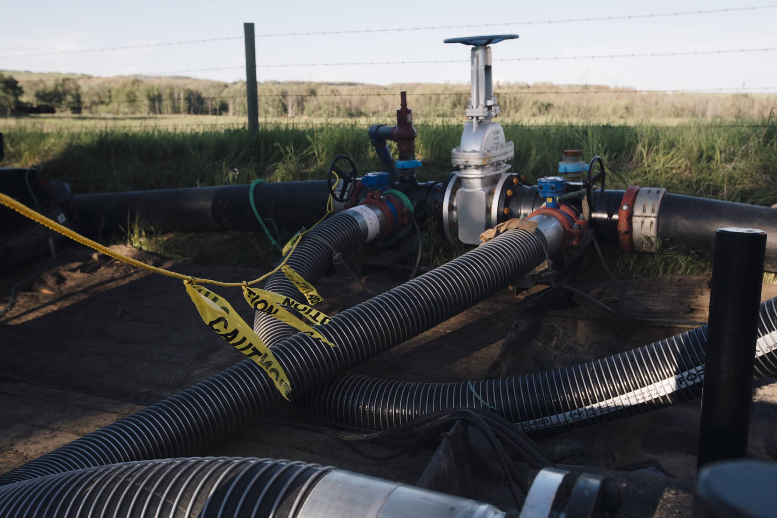 A pump and valve system in a ditch off a prairie road with green fields in the background.