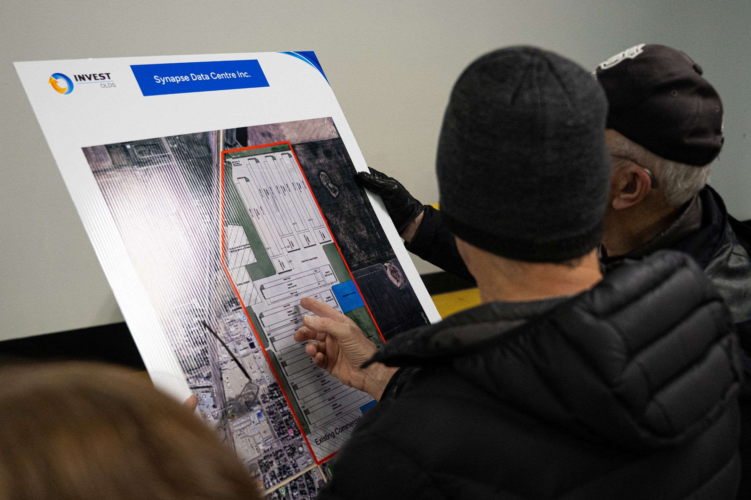 People look at and point to a diagram of a proposed AI data centre printed on a poster board.