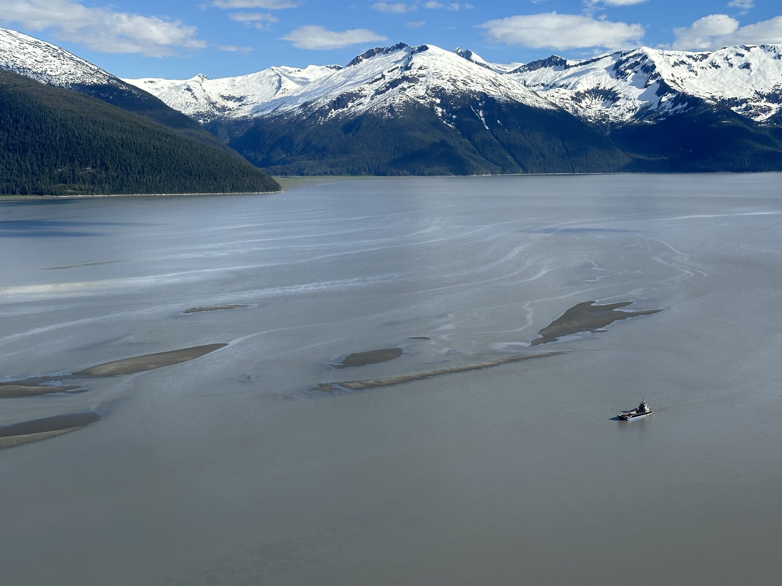 A small barge wades through a contaminated river betwixt snowy mountains.