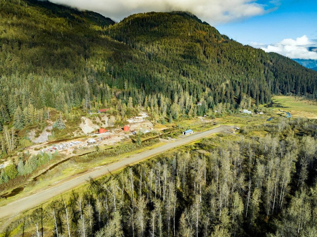 Small house structures line a small dirt road on the side of a tree-dense mountainside.