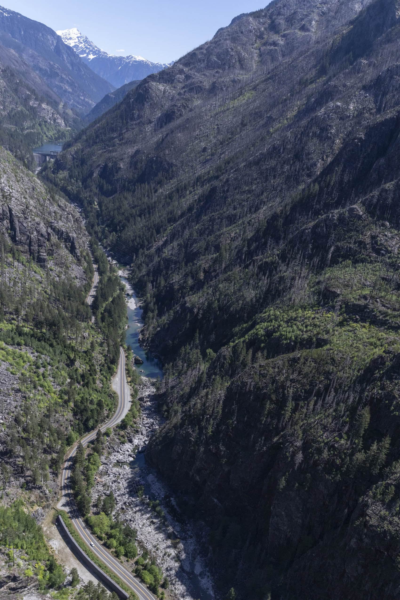 An aerial view of a mostly empty river channel next to a highway in a mountainous region.