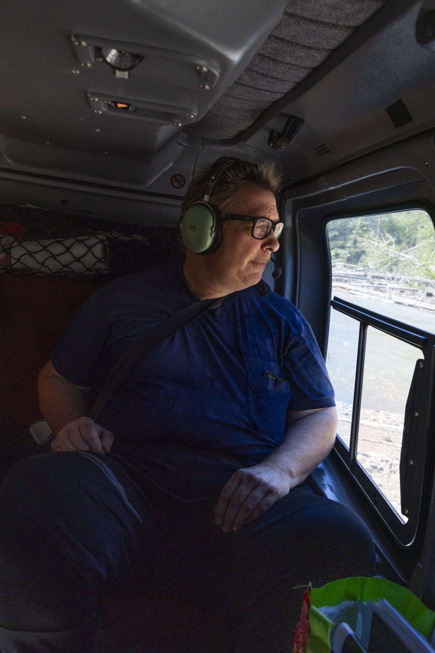 A person wearing large headphones looks out the window of a helicopter.