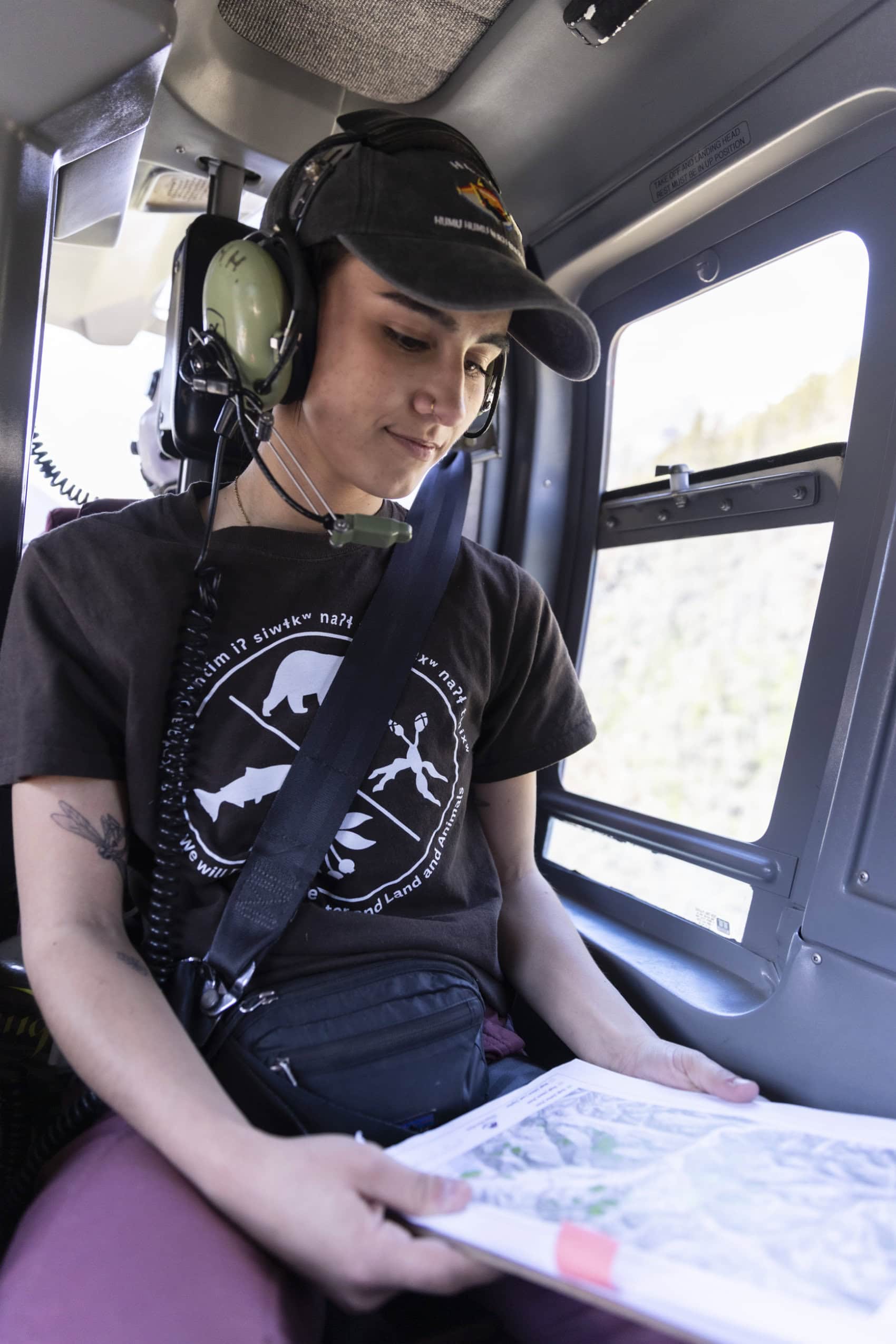 A person wearing large headphones looks down at a map while sitting in a helicopter.