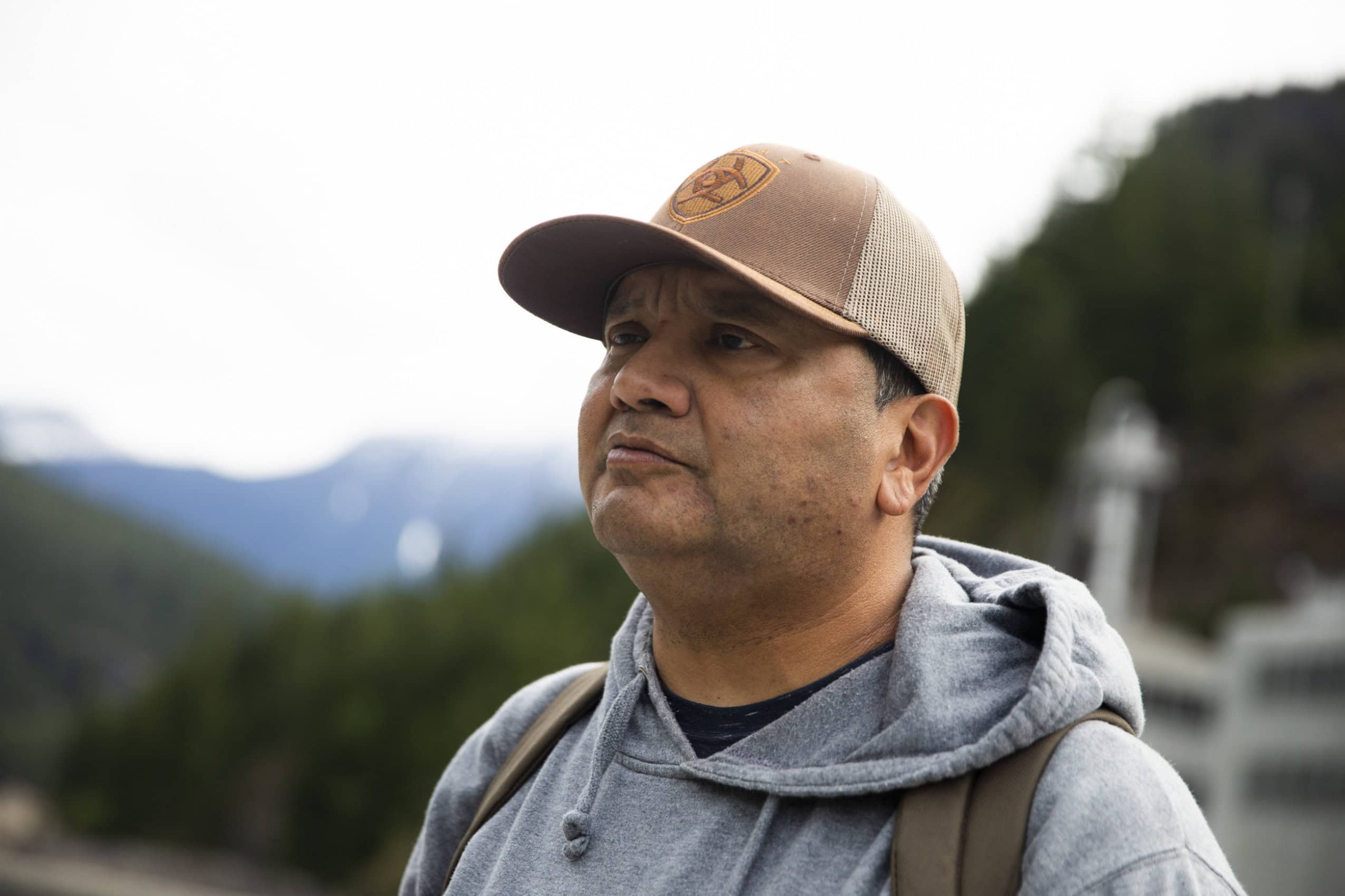 A portrait of Upper Skagit Tribe member Scott Schuyler. He is wearing a ball cap and hoodie and looking toward the left.