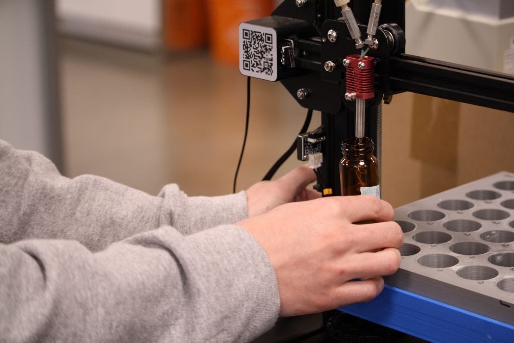 A woman's hands holding a water sample tube under a machine.