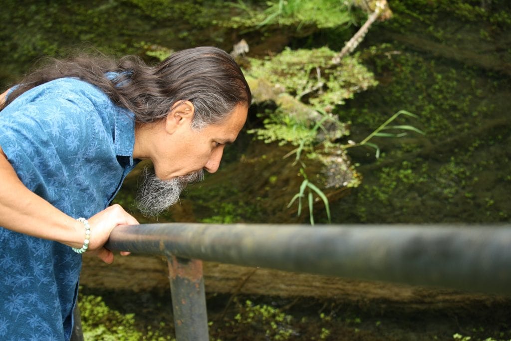 A man bending over a river and looking down into it.