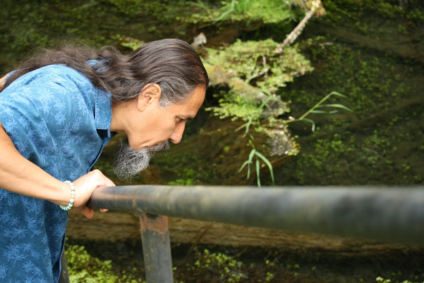 A man bending over a river and looking down into it.