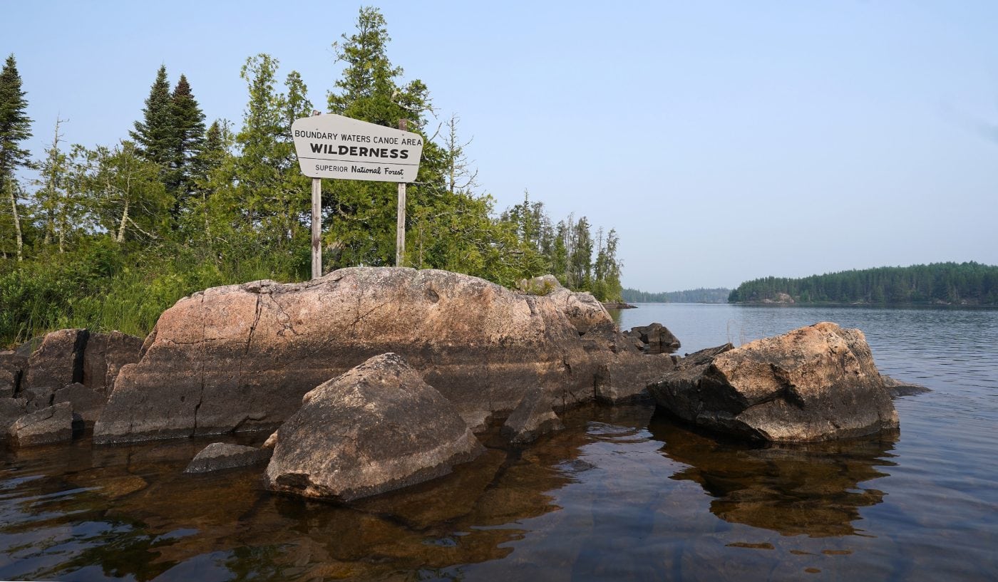 A sign on a rocky outcrop by a body of water welcomes paddlers to the Boundary Waters Canoe Area Wilderness.