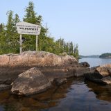 A sign on a rocky outcrop by a body of water welcomes paddlers to the Boundary Waters Canoe Area Wilderness.