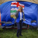 Alberta Premier Danielle Smith stands in front of a large Alberta flag as it blows in the wind.