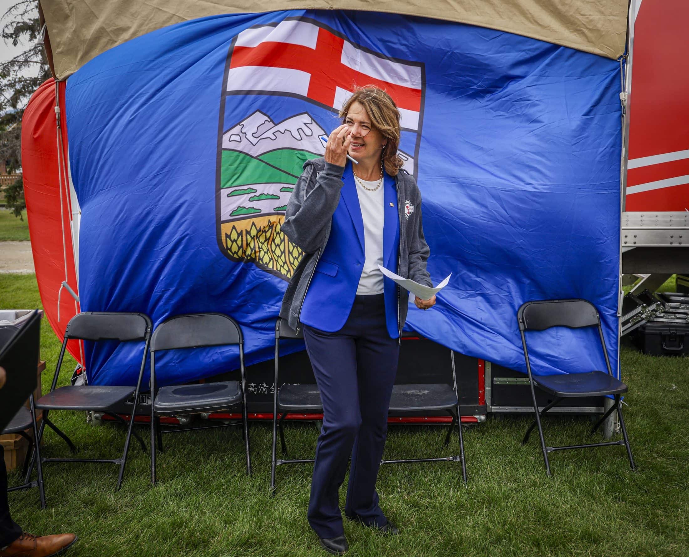 Alberta Premier Danielle Smith stands in front of a large Alberta flag as it blows in the wind.
