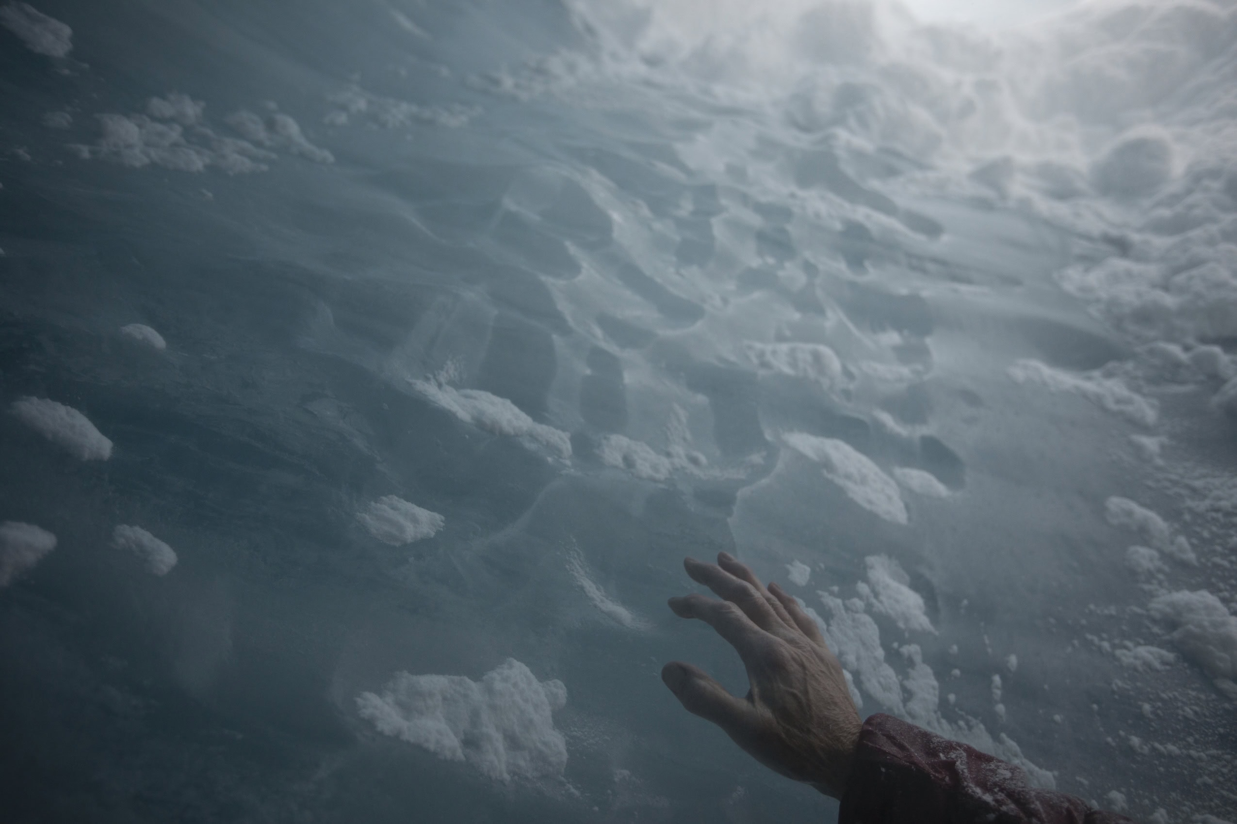 A hand reaches out and touches a wall of ice.