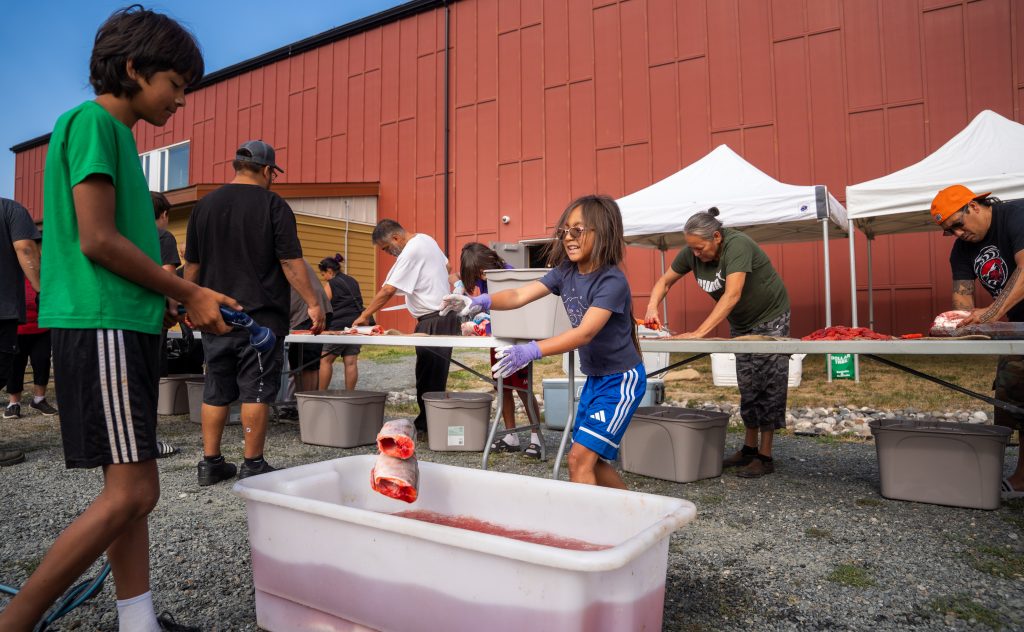 Youth wash sockeye salmon off with water after being gutted during a community fish canning day.