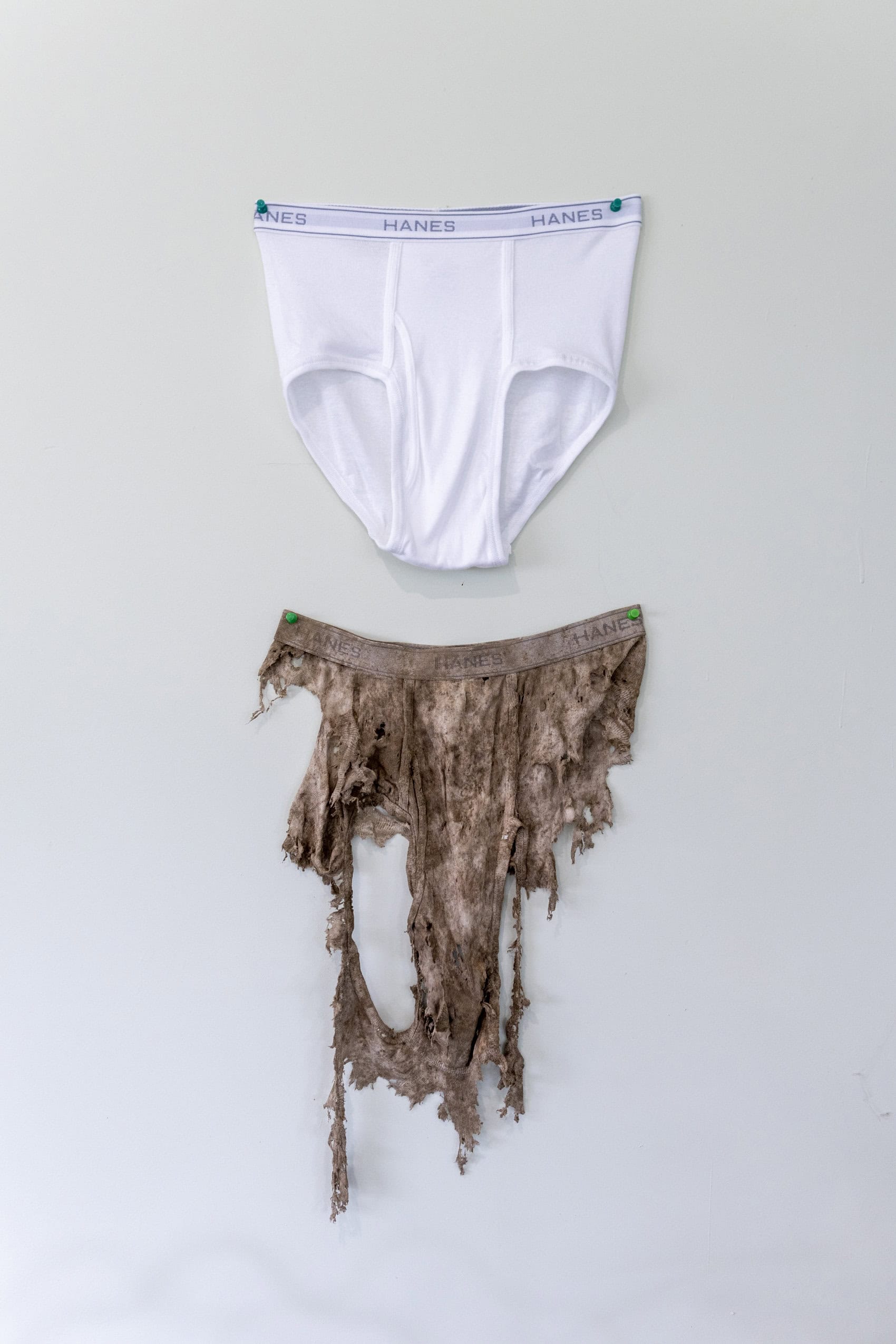 A pair of clean white men's underwear hangs on the wall above a pair of torn up and dirt-stained underwear