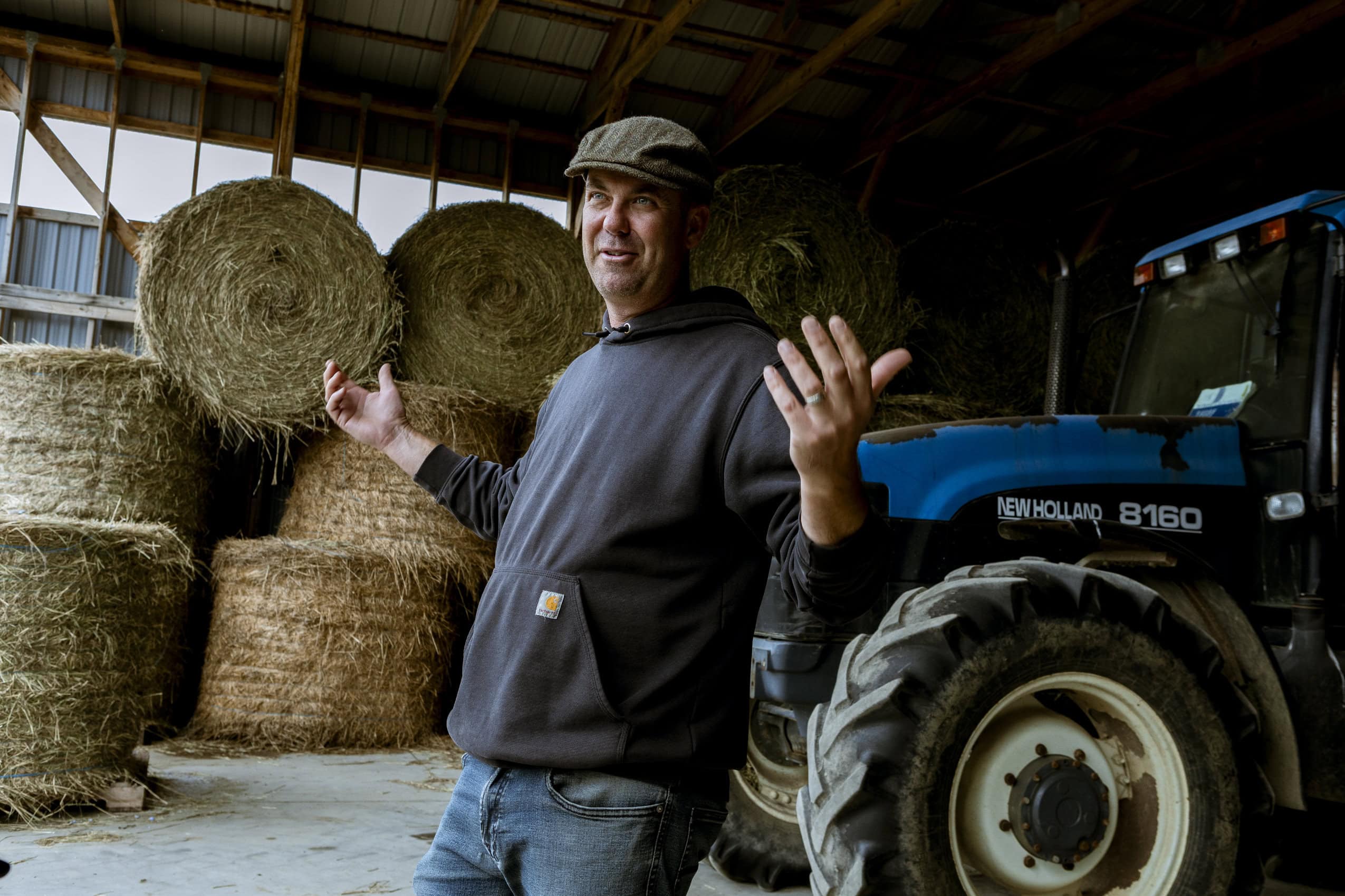 Norm Lamothe stands in front of a tractor, with hay bales behind him