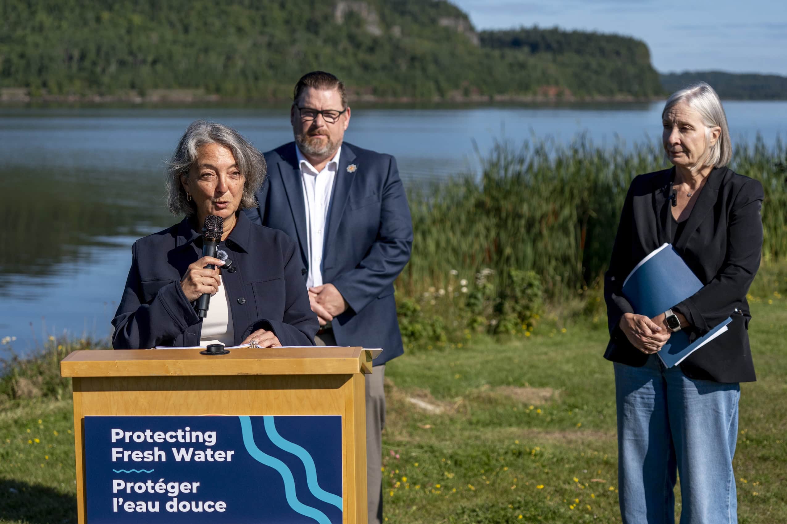 Canada’s Minister of Environment, Julie Dabrusin speaks at a podium with Nipigon Bay, on Lake Superior, behind her