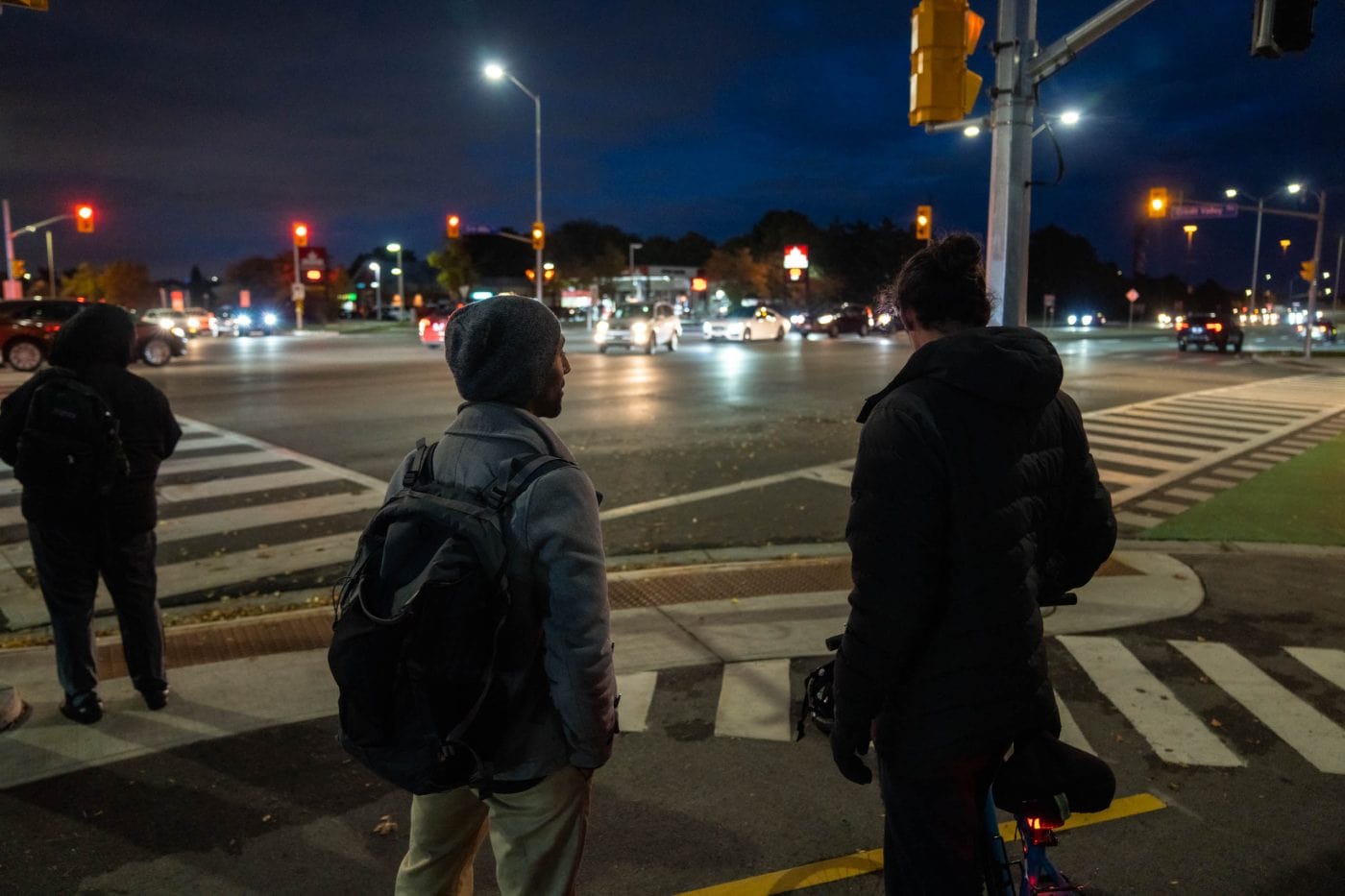 Photo from behind of two people facing an intersection with a gas station in the background.