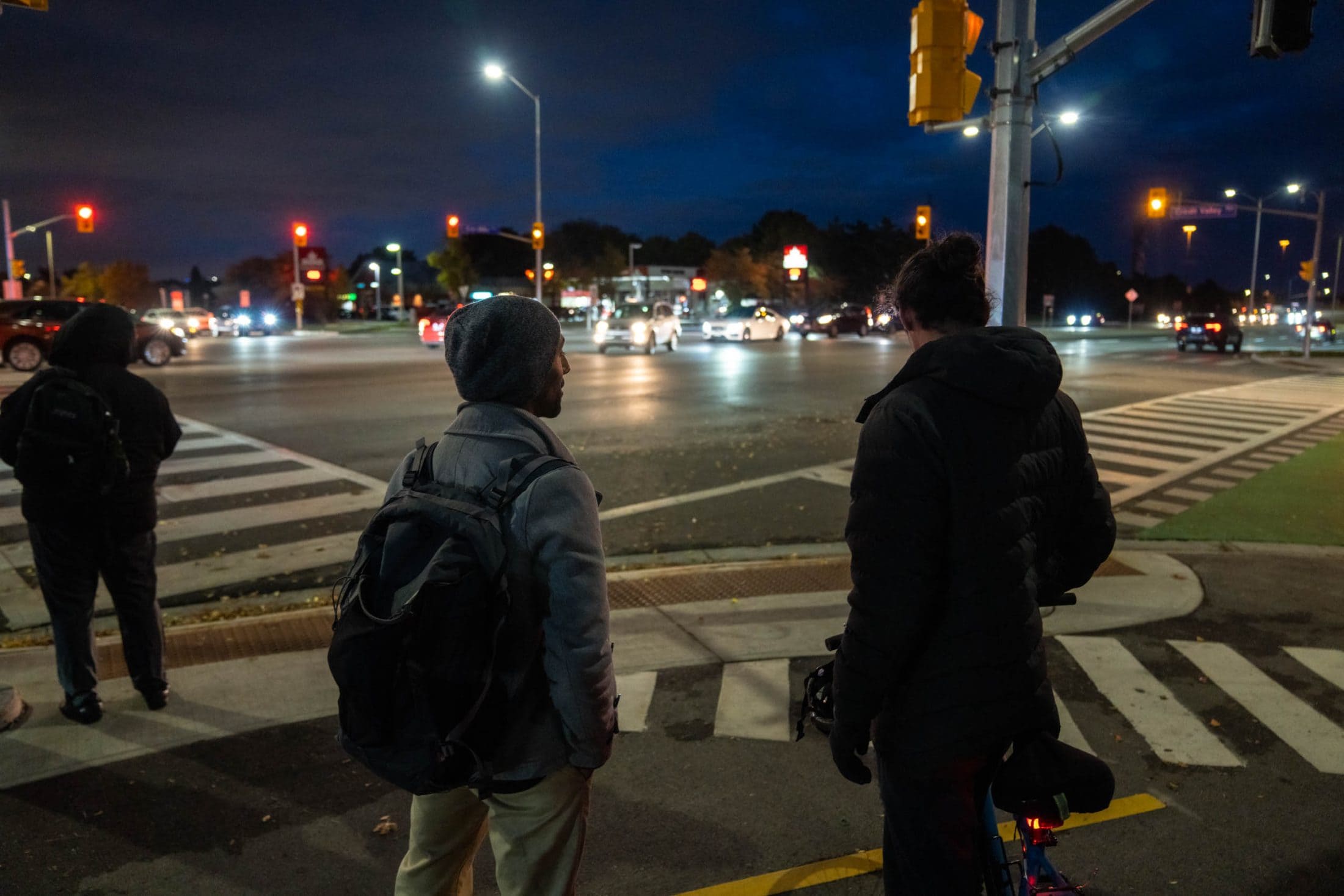 Photo from behind of two people facing an intersection with a gas station in the background.