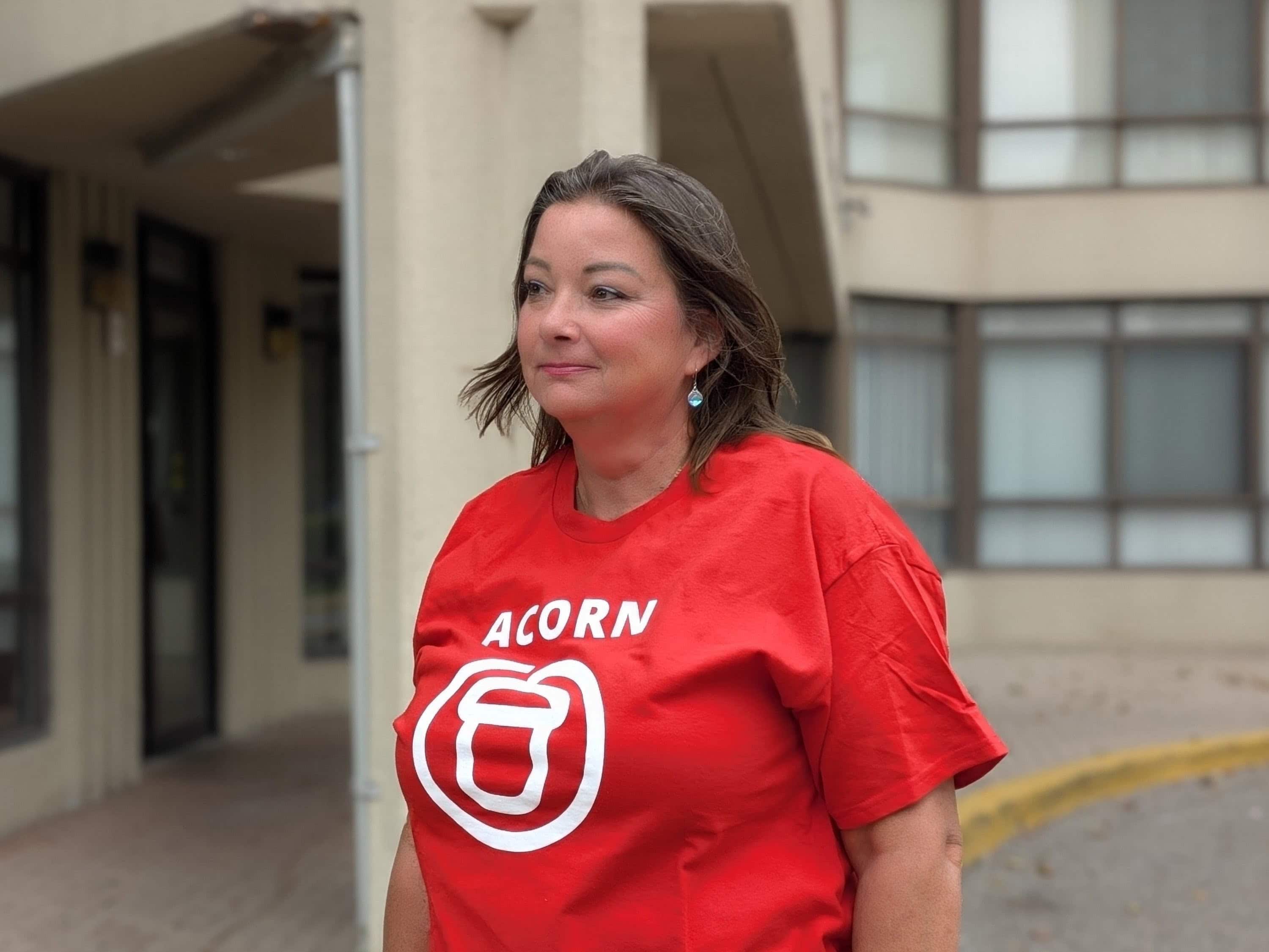 A woman looks to the side wearing an ACORN t-shirt
