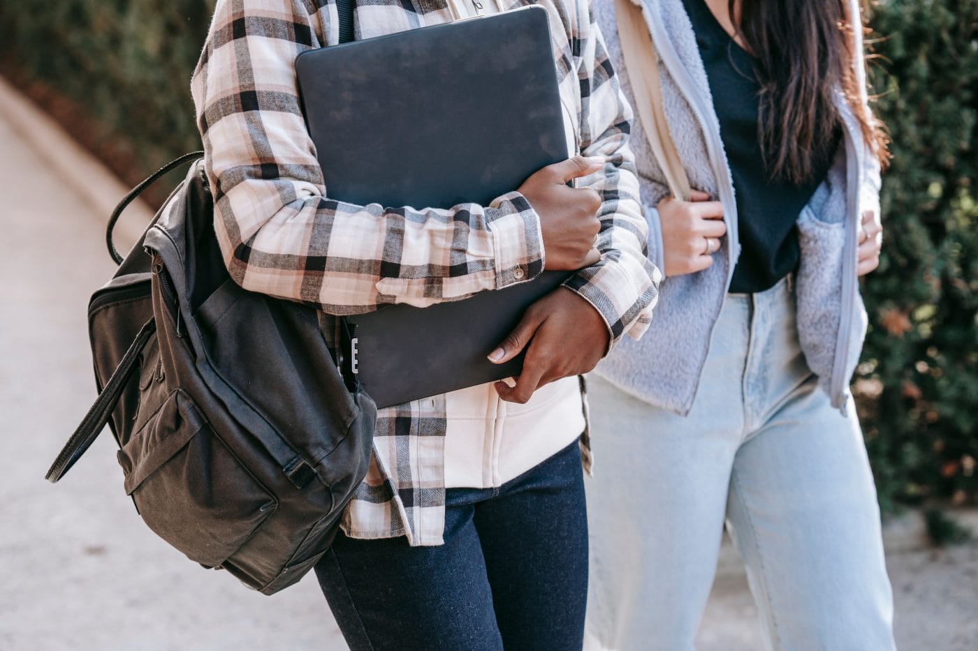 Two students carrying backpacks and books walk down a street