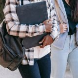 Two students carrying backpacks and books walk down a street