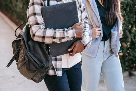Two students carrying backpacks and books walk down a street