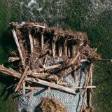 Seen from above, a pile of logs and other wood debris in the middle of a relatively shallow flowing river.