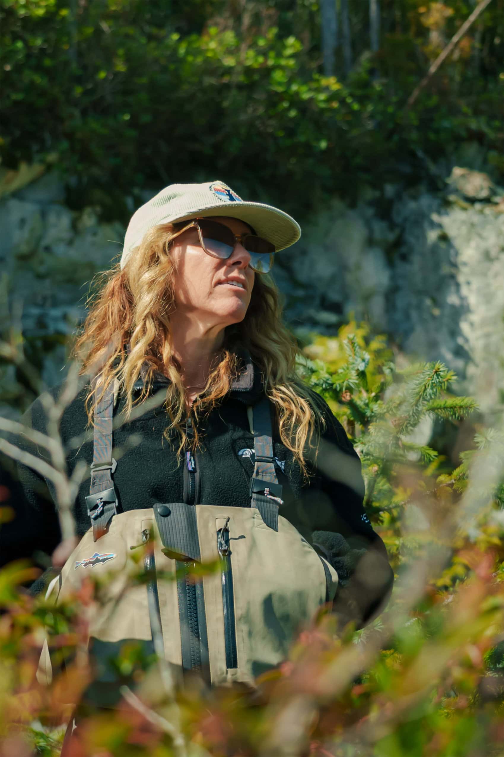 Jessica Hutchinson is photographed wearing sunglasses, chest waders and a ball cap and looking off into the distance.