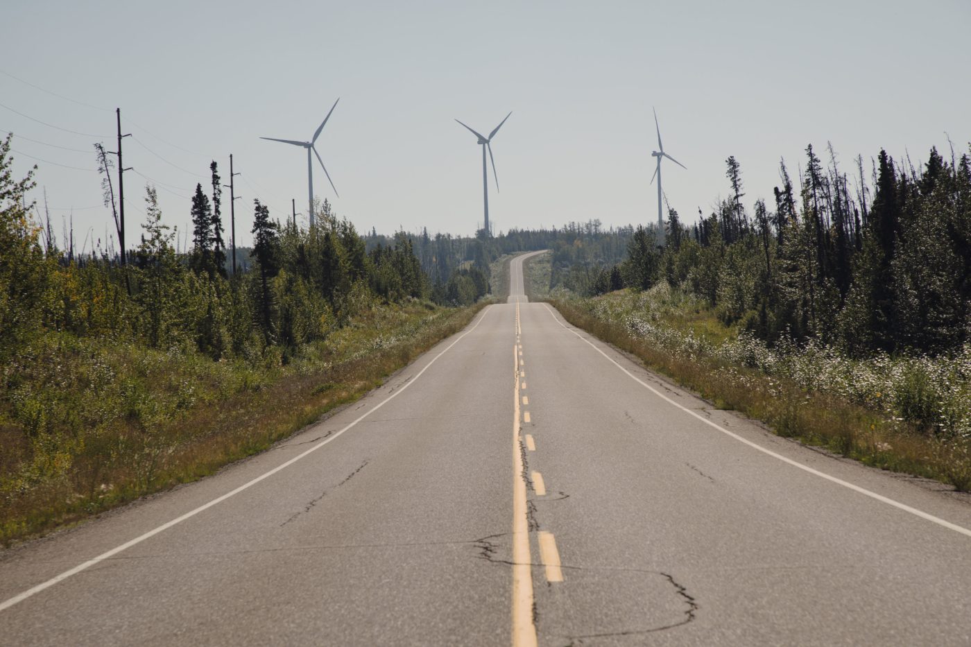A two-lane highway recedes into the distance, where wind turbines stand on the horizon.